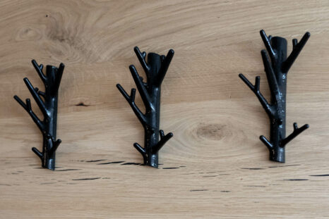 Nahansicht Design Kleiderhaken, schwarz lackiert, vor heller Naturholzwand.