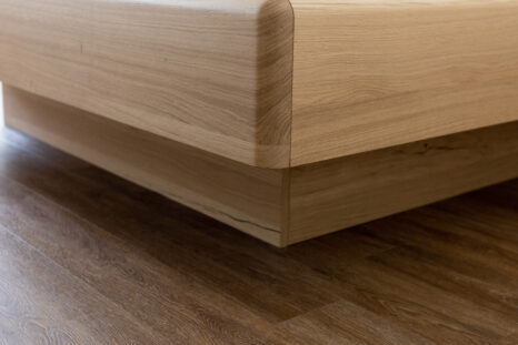 Nahaufnahme rechte untere Ecke von hellem Naturholzbett auf hellem Vinylboden in Holzoptik.