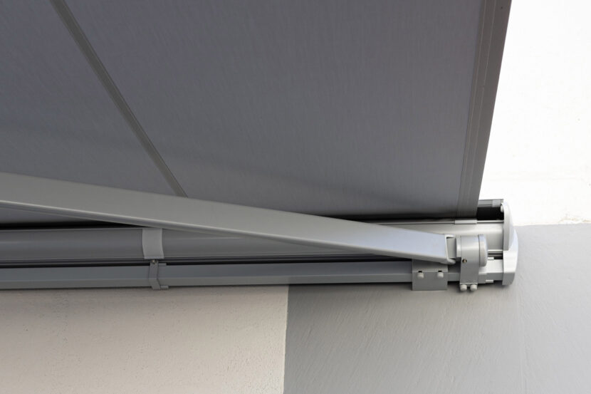 Blick von vorne unten auf ausgefahrene Kassettenmarkise, Gelenkarme weiß lackiert.