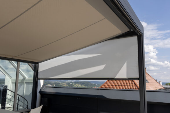 Blick von der Seite auf Q-Bus mit schwarzem Metallrahmen, beiges Segel und weißer Volant ausgefahren.