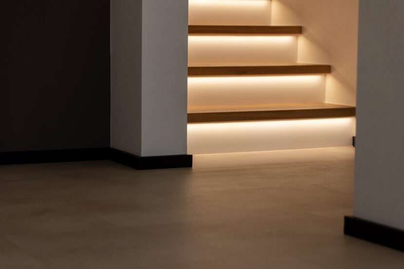 Nahansicht Mineralboden und weiße, beleuchtete Treppe in Obergeschoss.