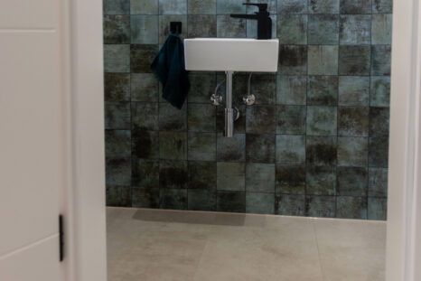 Mineralboden in WC, weißes Waschbecken und seegrüne Fliesenwand im Hintergrund.