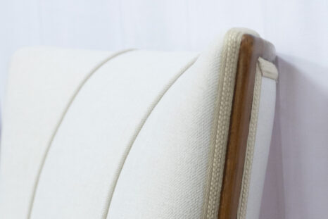 Detailansicht frisch aufgepolsterte Lehne mit weißem Polster, dunkler Holzrahmen, Goldbordüre.