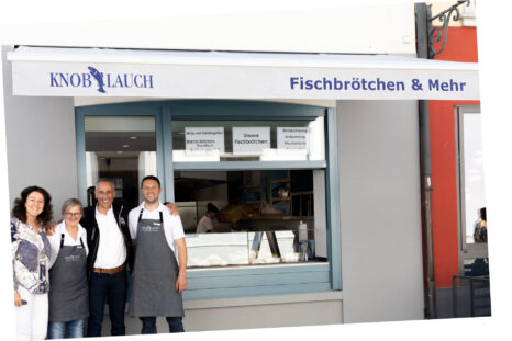 Sicht von vorne auf Ladenfront von Fischverkauf Knoblauch, weiße Markise ausgefahren, Firmenname auf Volant in blauer Schrift.