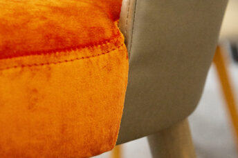 Frisch gepolsterter Barhocker in Nahansicht, links im Vordergrund das orangene Velourspolster, rechts daneben graue Lehne.