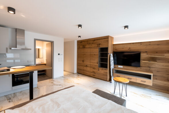 Wohnzimmer neu eingerichtete Ferienwohnung mit dunklen Naturholzschränken, weißen Wänden und Deckenstrahlern.
