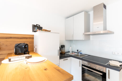 Küchenzeile neu eingerichtete Ferienwohnung mit hellem Naturholztisch, weißen Wänden und Holzvertäfelung an einer Wand.