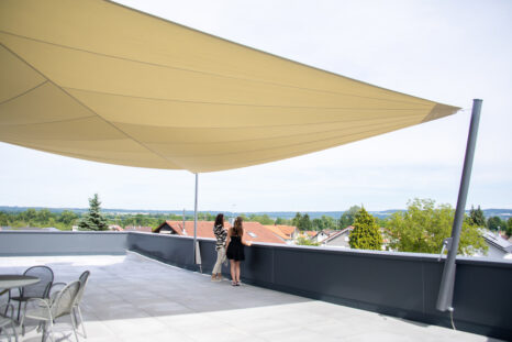 Dachterrasse in Gesamtansicht, hell beiges Sonnensegel ist über die ganze Terrasse gespannt, im Hintergrund Ortschaft Staig.