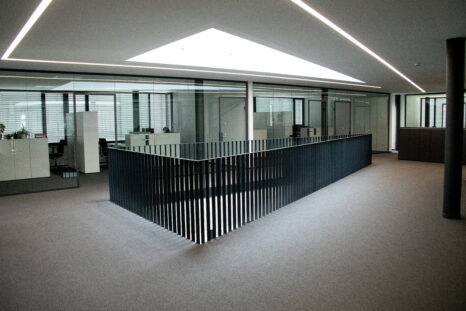 Atrium mit frisch verlegten Teppichfliesen und schwarzem, metallenen Treppengeländer mittig, im Hintergrund Glastüren.