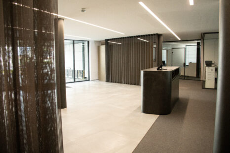 Empfangsraum mit Übergang von hellgrauen Teppichfliesen zu weißem Steinboden.