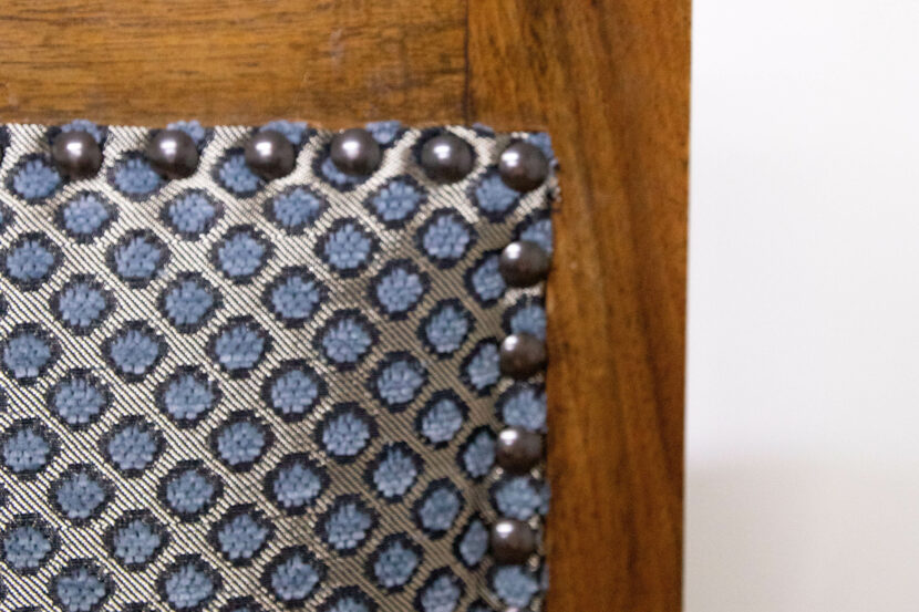 Nahaufnahme der Rückenlehne des frisch gepolsterten, geschnitzten Stuhls. Das neue Polster ist weiß mit aquamarinblauen, schwarz umrandeten Punkten.