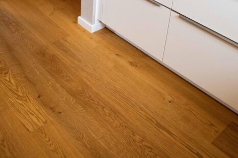 Ansicht von oben auf Echtholzparkett, im Hintergrund weiße Schubladenkommode.