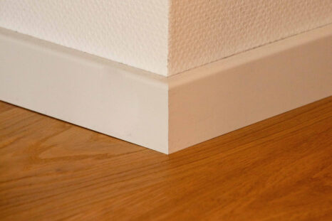 Nahansicht Raumecke, weiße Sockelleisten vor weißer Wand, Echtholzparkett.