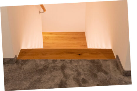 Blick von oben auf Treppe, im Vordergrund der neue dunkle flauschige Teppich, die Wände sind weiß.