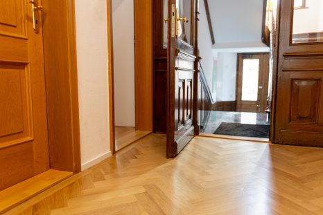 Frisch verlegter Fischgrätparkettboden, links im Bild ist eine Tür aus hellem Holz, das Bild ist zur Treppe hin orientiert.