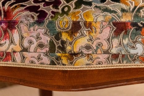 Nahansicht der mittigen Sitzkante des frisch aufgepolsterten Armlehnenstuhls. Samtstoff mit floralem Muster, der Stuhl befindet sich vor weißem Hintergrund.