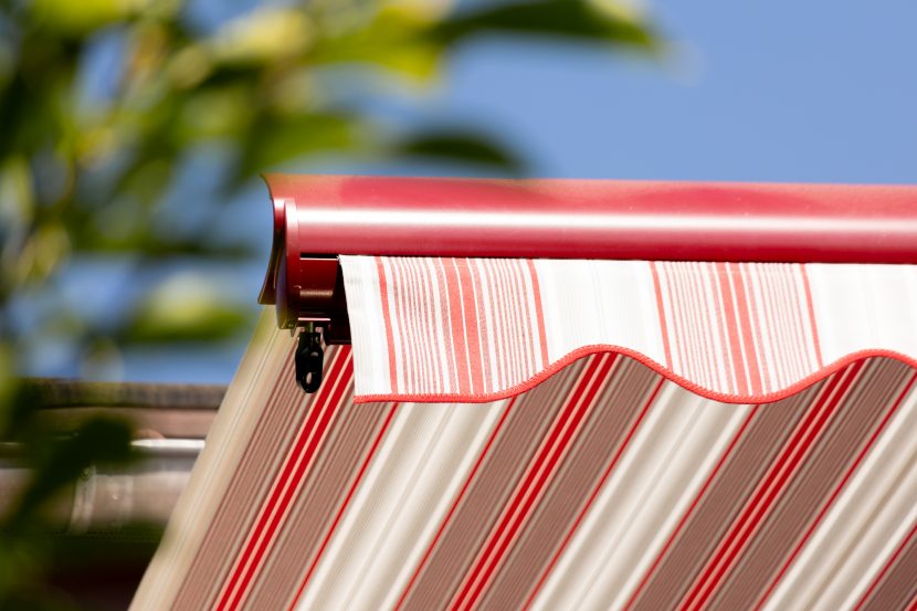 Detailansicht der Kante einer ausgefahrenen rot-weiß gestreiften Kassettenmarkise vor blauem Himmel.