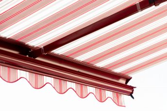 Innenansicht 3/4 Perspektive einer ausgefahrenen Kassettenmarkise, rot-weiß gestreift mit rot lackiertem Markisenarm.