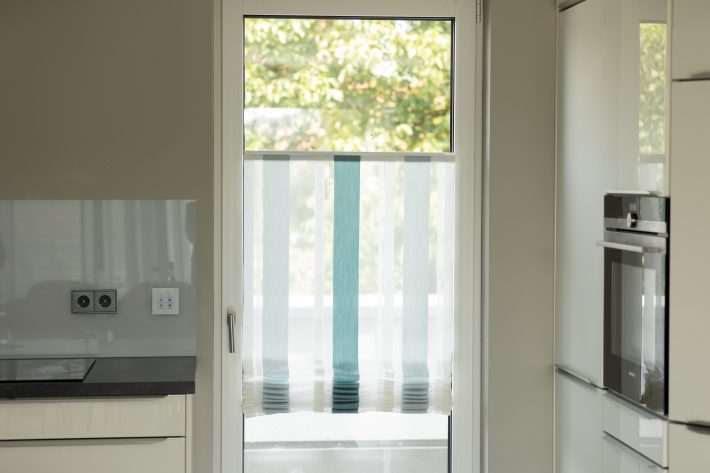 Totale von Balkontür, weiß, mit blau-weiß gestreiften Aeros, links im Bild ist eine Küchenplatte, rechts ein Kühlschrank zu sehen.