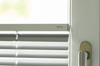 Nahansicht von Innenjalousien, der Fensterrahmen ist weiß, der Fenstergriff ist rechts im Bild zu sehen.