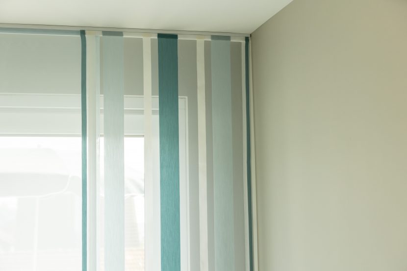 Ansicht obere Raumecke, weiße Wände, blau-weiß gestreifte Aeros an Schiene vor weißem Fensterrahmen.