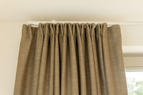 Ansicht frontal unten geraffte neue hellbraune Gardinen vor weißer Fensterfront.