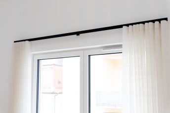 Weißes Doppelfenster, schwarze Gardinenschiene von Haller mit cremeweißen Wellenvorhängen.