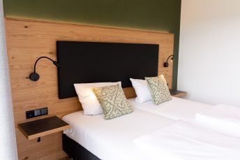 Hotelzimmer Sennerbad eingerichtet von Haller Raumgestaltung, Sicht auf weiß bezogenes, geschreinertes Doppelbett vor heller Holzvertäfelung.
