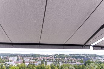 Ansicht komplett ausgefahrene weißgraue Doppelmarkise mit anthrazitfarbenem Gehäuse vor Stadtpanorama, installiert in Hotel Sennerbad Ravensburg.