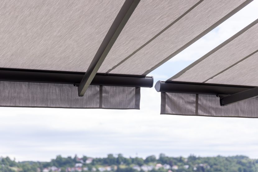 Dreiviertelansicht von hinten weißgraue Doppelmarkise, ausgefahren, mit anthrazitfarbenem Gehäuse und leicht ausgefahrenem Volant, installiert in Hotel Sennerbad Ravensburg.