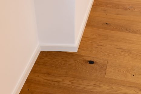 Schräg von oben Ansicht auf neues Eichenparkett, weiße Wände mit doppelter Ecke und weißer Sockelleiste.